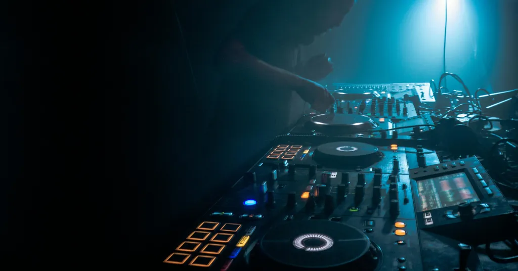 DJ mixing console with turntables, control panels, and blue stage lighting in dark venue.