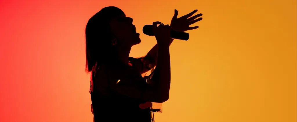 Silhouette d'une personne chantant dans un micro sur un fond dégradé orange et rouge vibrant.