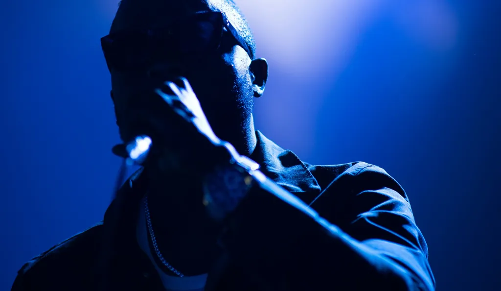 Silhouetted figure in a dimly lit blue-toned scene, with hands gesturing against a bright background.