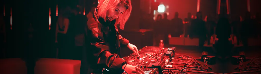 Person in dark clothing kneeling on ground working with equipment, illuminated by red lighting in dimly lit indoor space.