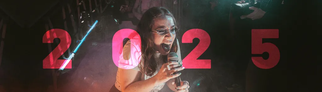 Mulher com óculos segura microfone, números "2025" em vermelho e rosa ao fundo com efeitos de luz coloridos.