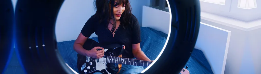 Woman with long dark hair in black outfit playing electric guitar inside large circular white and blue structure with geometric lighting.