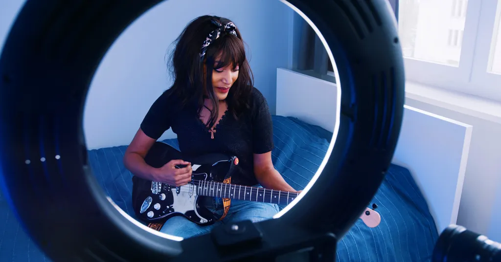 Frau mit dunklen Haaren spielt E-Gitarre, gerahmt durch kreisförmiges Ringlicht in blau beleuchteter Umgebung.
