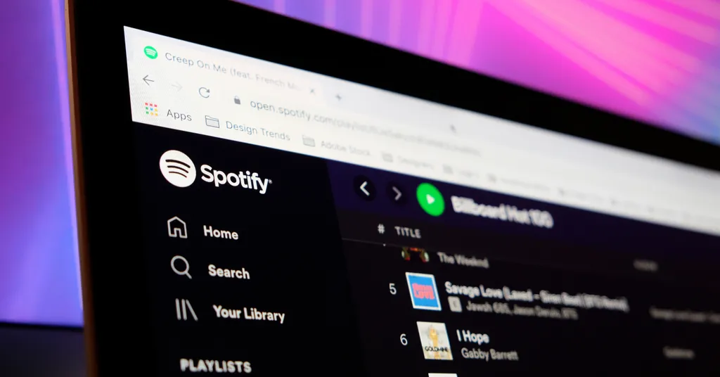 Écran d'ordinateur affichant l'interface Spotify avec menu de navigation à gauche et liste de lecture, fond violet-rose flou.