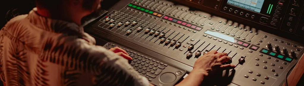 Tonmischpult mit vielen Reglern und Bedieneinheiten, mit dem ein Tontechniker arbeitet.