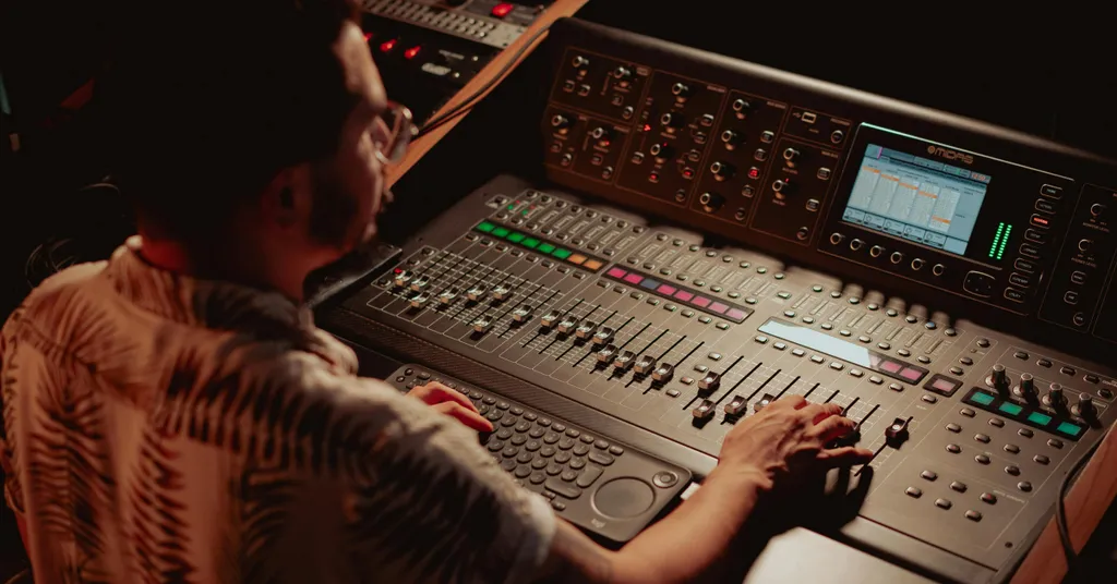 Mastering Engineer, der an einem professionellen Mischpult arbeitet, das mit Reglern, Anzeigen und einer Bildschirmoberfläche ausgestattet ist.