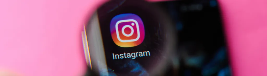 Smartphone screen showing Instagram app icon with gradient pink-to-orange circular logo on pink background surface.