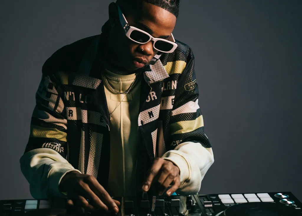 A person wearing sunglasses, a jacket with bold graphics, and holding a keyboard synthesizer.
