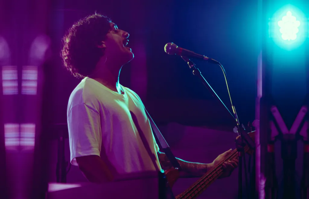 Musician singing into microphone while playing guitar under bright blue stage lights with purple lighting in background.