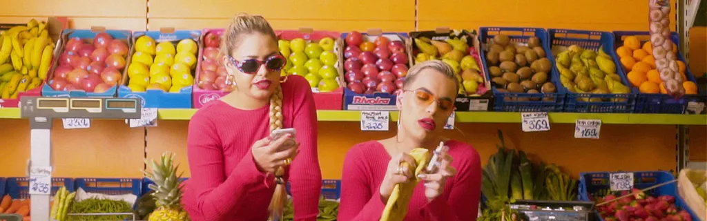 two blond women in pink in front of a fruit stand