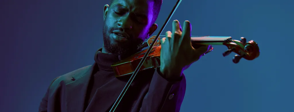 Um homem tocando violino com iluminação colorida no palco.