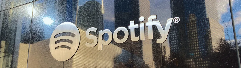 White Spotify logo and text on glass window with city buildings reflected in background.