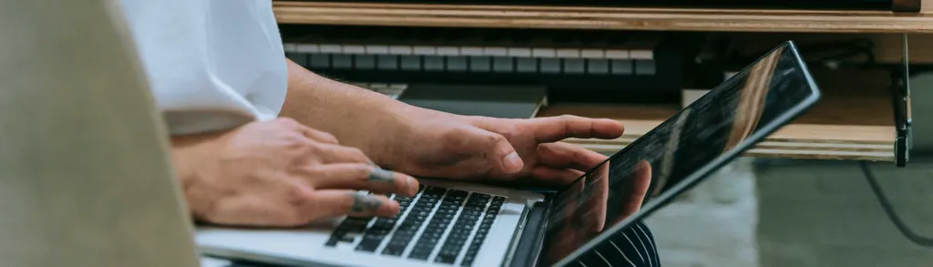 Person's hands typing on laptop keyboard with books stacked in background on desk.