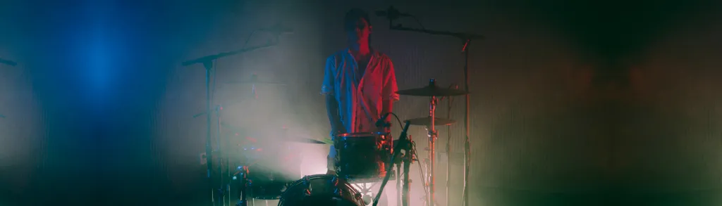 Person in red hoodie stands in smoky room with blue and white stage lighting, silhouetted against hazy atmospheric conditions.