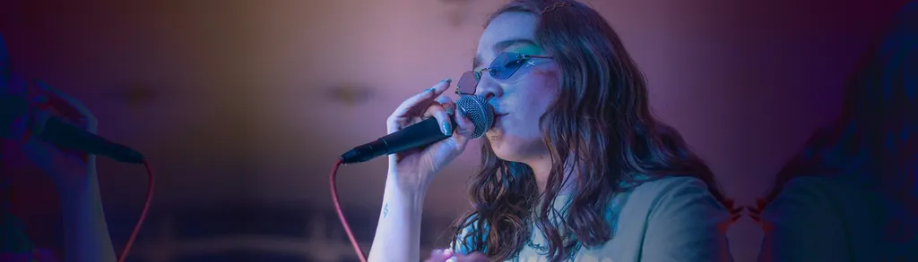 Woman with long hair singing into microphone under blue and purple stage lighting.