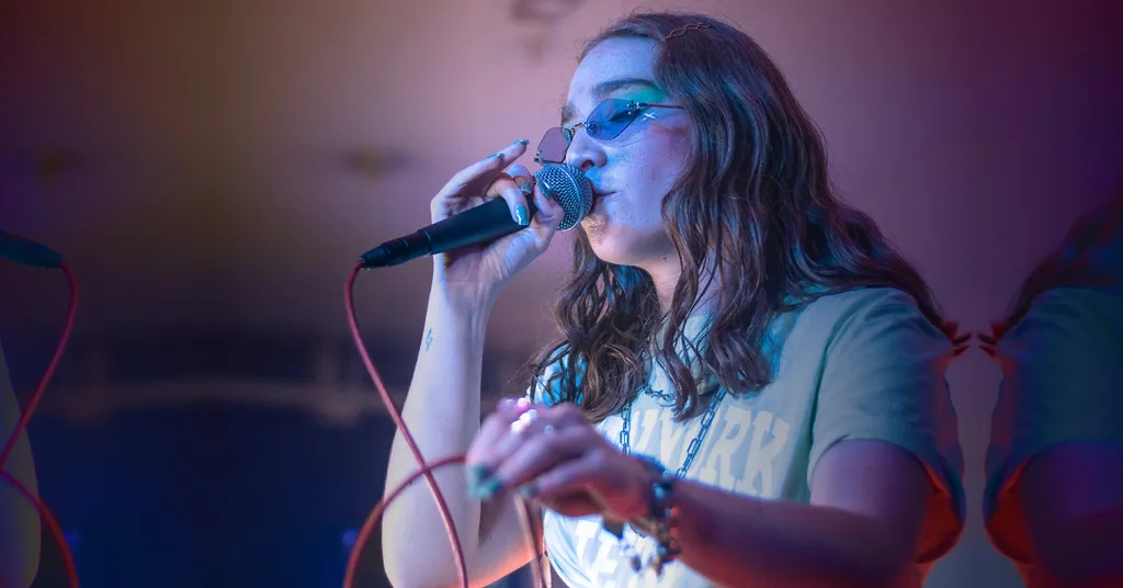 Woman with long hair singing into microphone on stage, lit with purple and blue stage lighting.