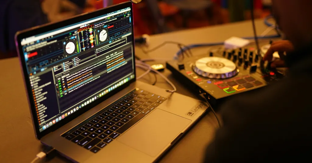 Laptop showing code on screen, DJ equipment in background.