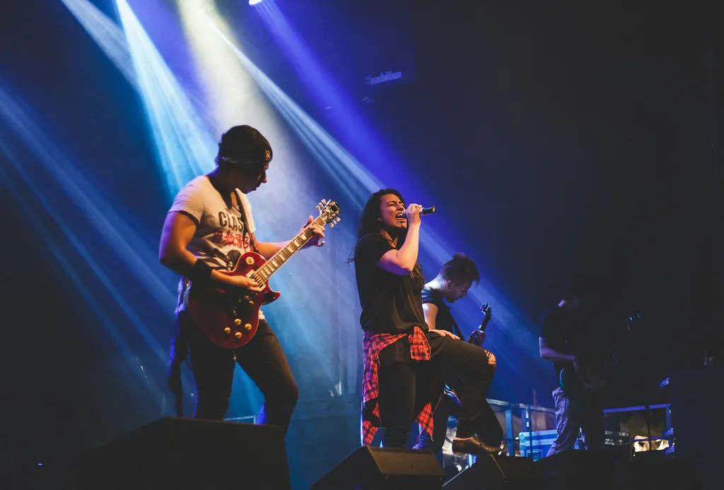Deux personnes sur scène jouant de la musique, avec un guitariste et un chanteur sur fond de lumières bleues et blanches.