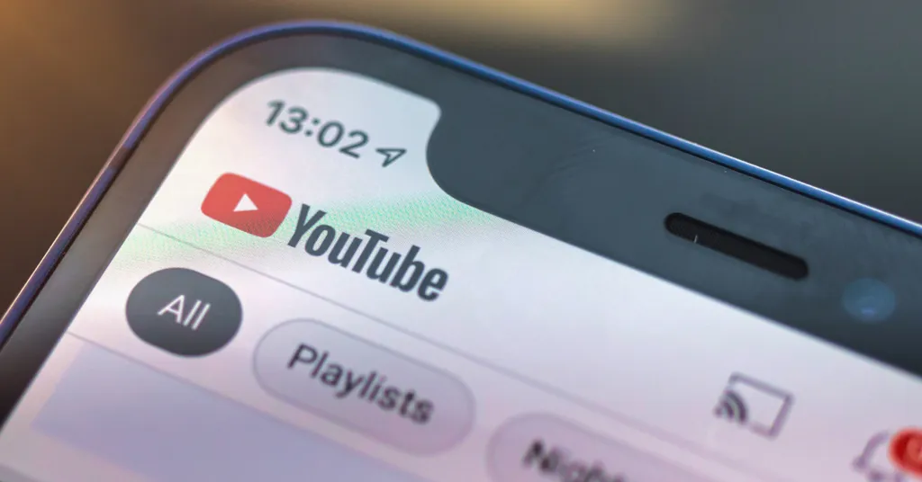 Pantalla de smartphone mostrando la aplicación YouTube con logo rojo, pestañas "All" y "Playlists", hora 13:02 visible arriba.