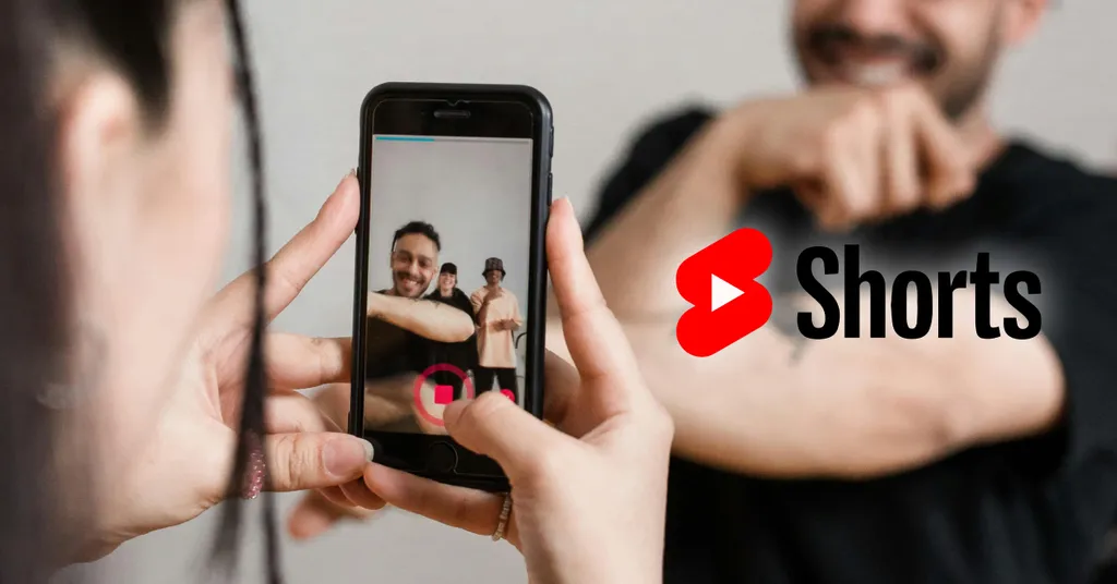 Hands holding smartphone recording two people, with YouTube Shorts logo overlay in red and black text on right side.