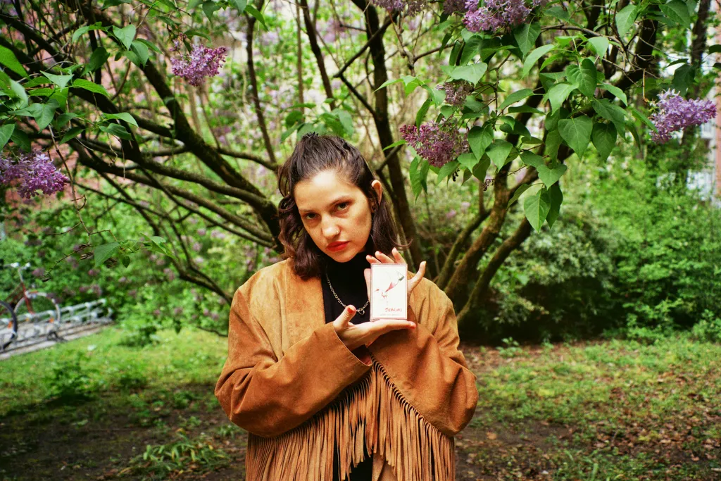 Adi Kum tenant une cassette devant un arbre en fleur
