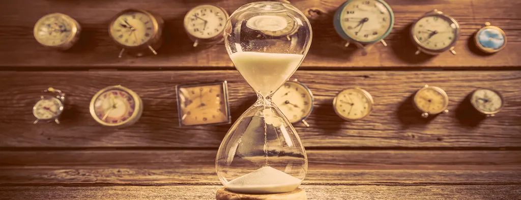 Reloj de arena con varios despertadores en el fondo